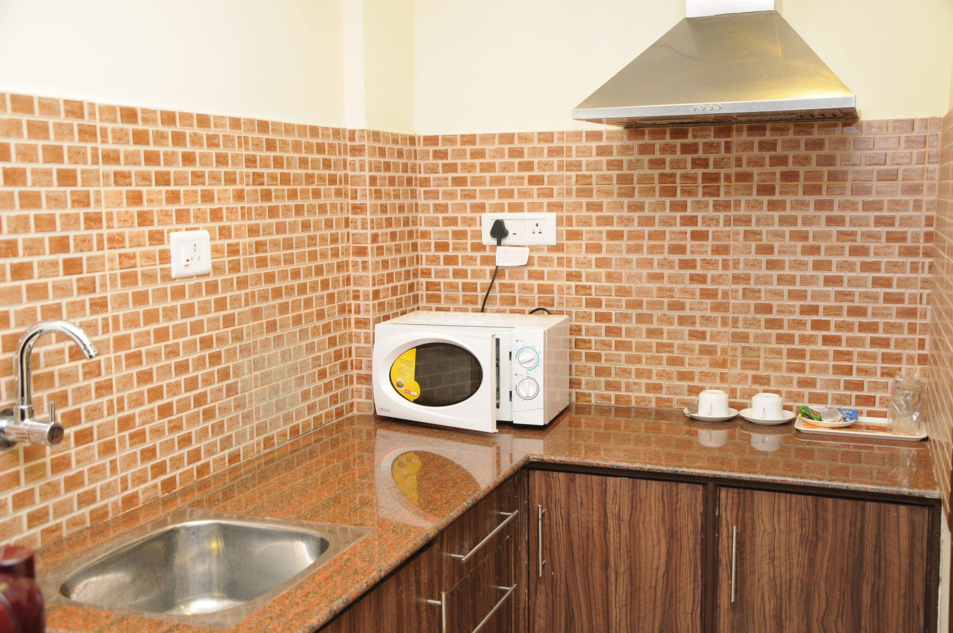 A kitchen with a microwave, a sink, and a countertop with a tray of cups and a glass.
