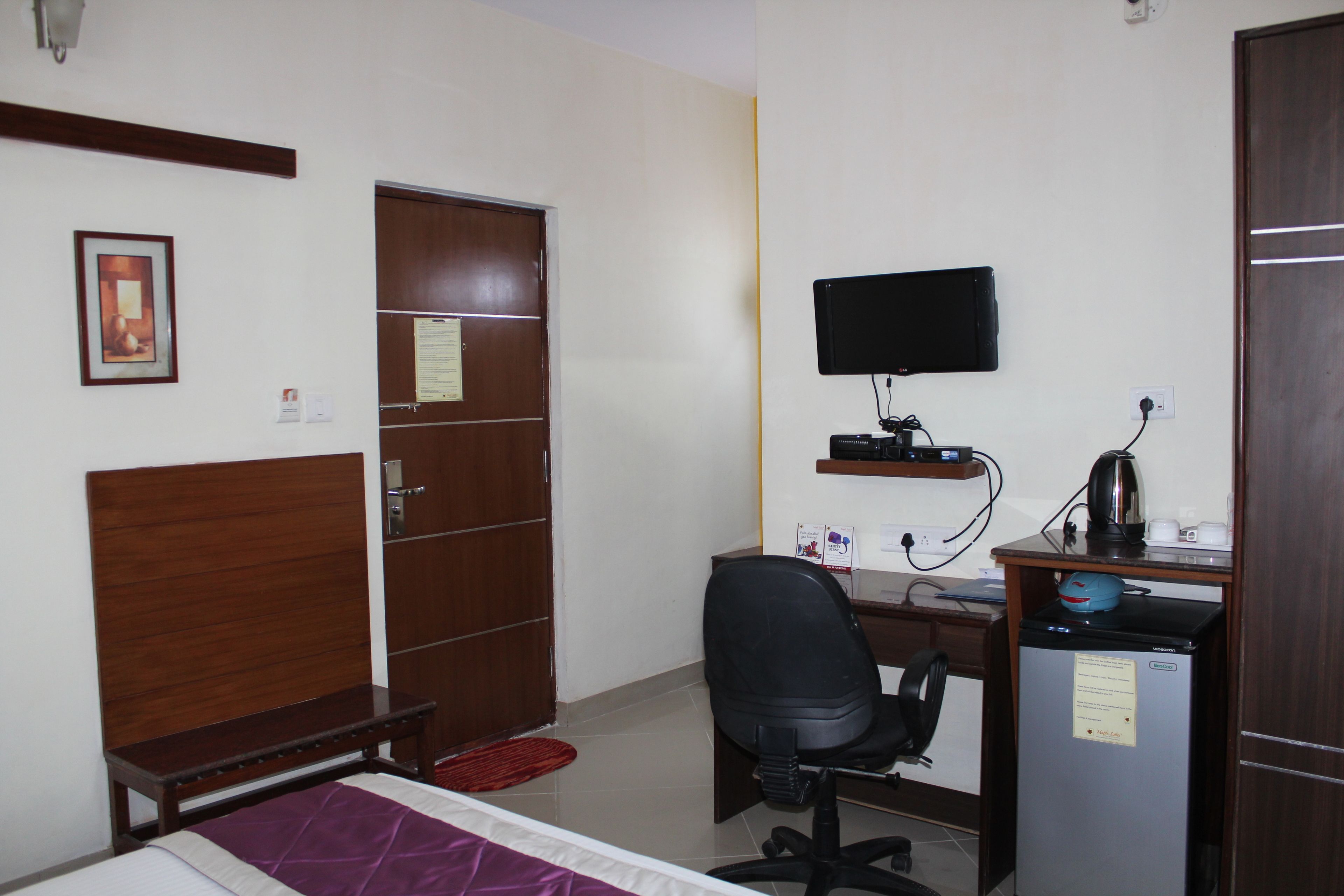 Habitación de hotel con cama, escritorio con computadora, silla, televisor montado en la pared y refrigerador.