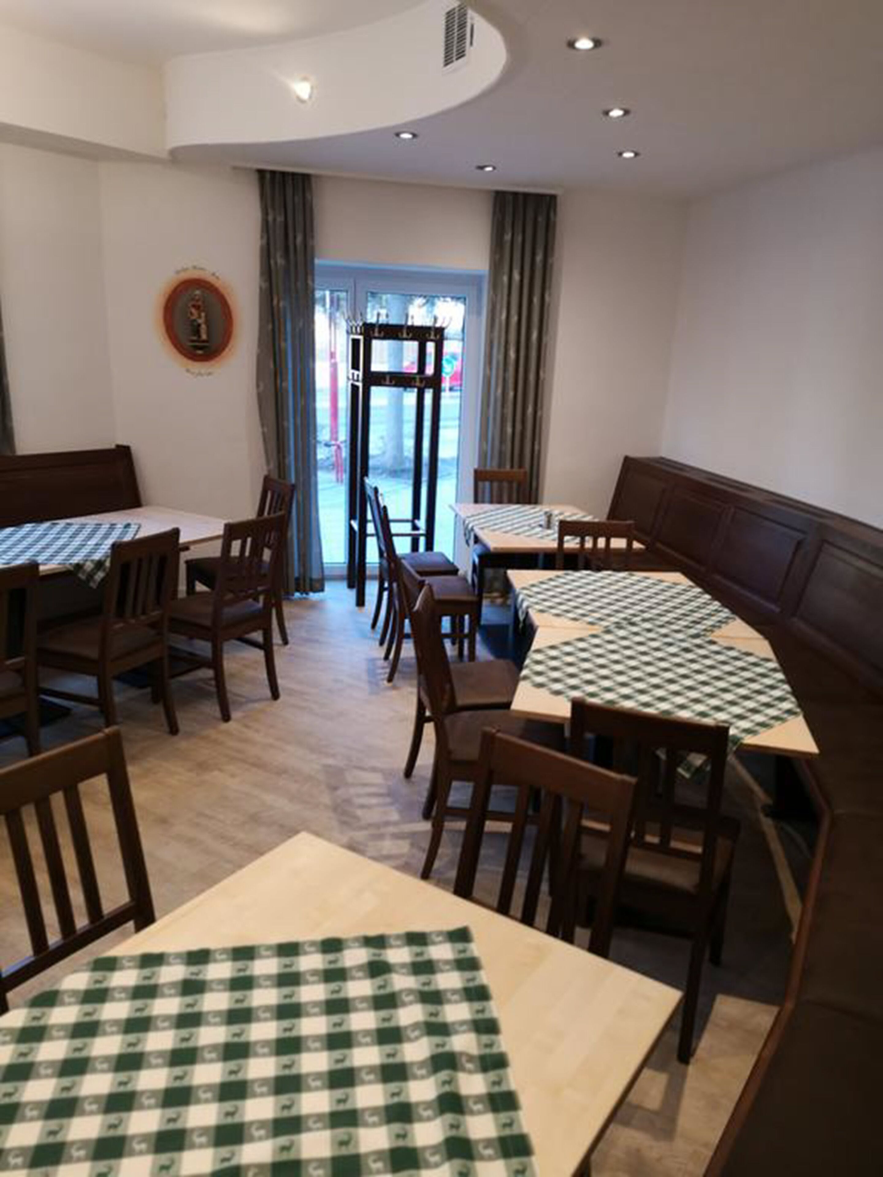 Interior de un restaurante con manteles a cuadros, sillas de madera y vistas a través de un ventanal.