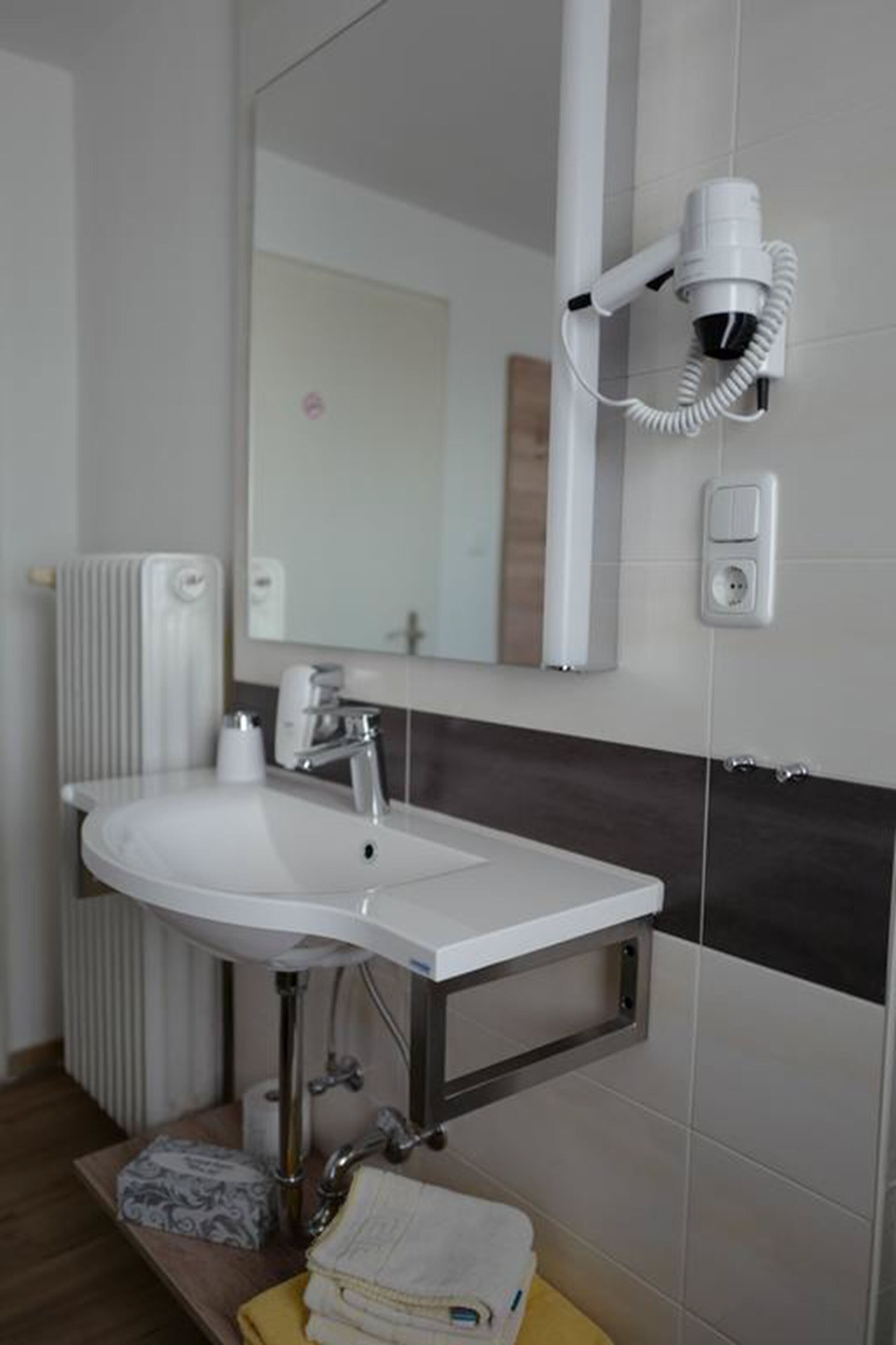 A bathroom with a white sink, a mirror, a hairdryer mounted on the wall, a towel rack, and a radiator.