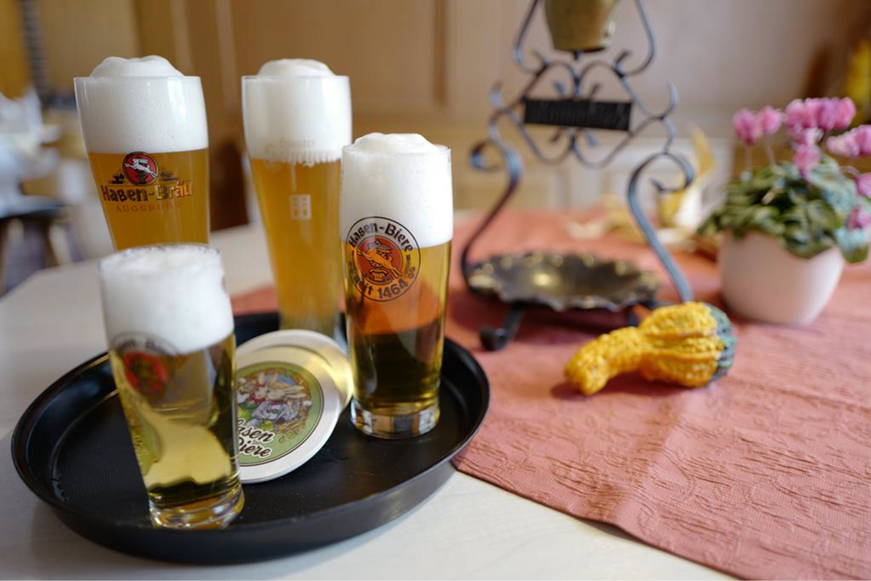 Four glasses of beer on a tray with a coaster, a metal stand, and a potted plant.
