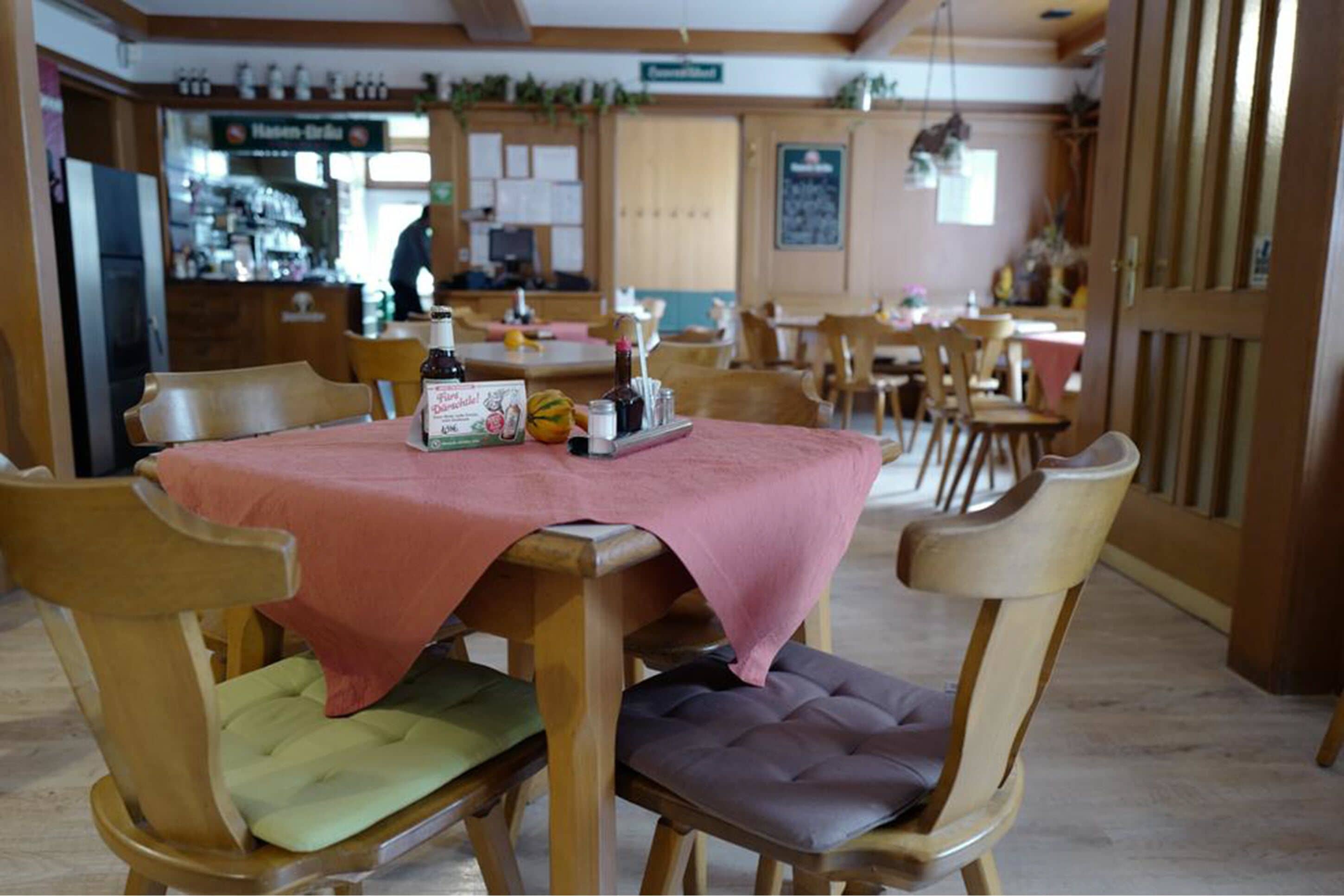 A restaurant with wooden tables and chairs, a bar area in the background, and a chalkboard menu on the wall.