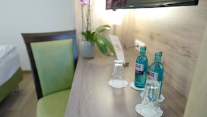 A hotel room with a wooden desk, a green chair, a small table with a vase of flowers, and a television mounted on the wall. - Hotel Gasthof Stern (Gersthofen)