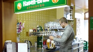 A bar area with a sign reading "Hassen-Brau Augsburg" and a bartender at work. - Hotel Gasthof Stern (Gersthofen)