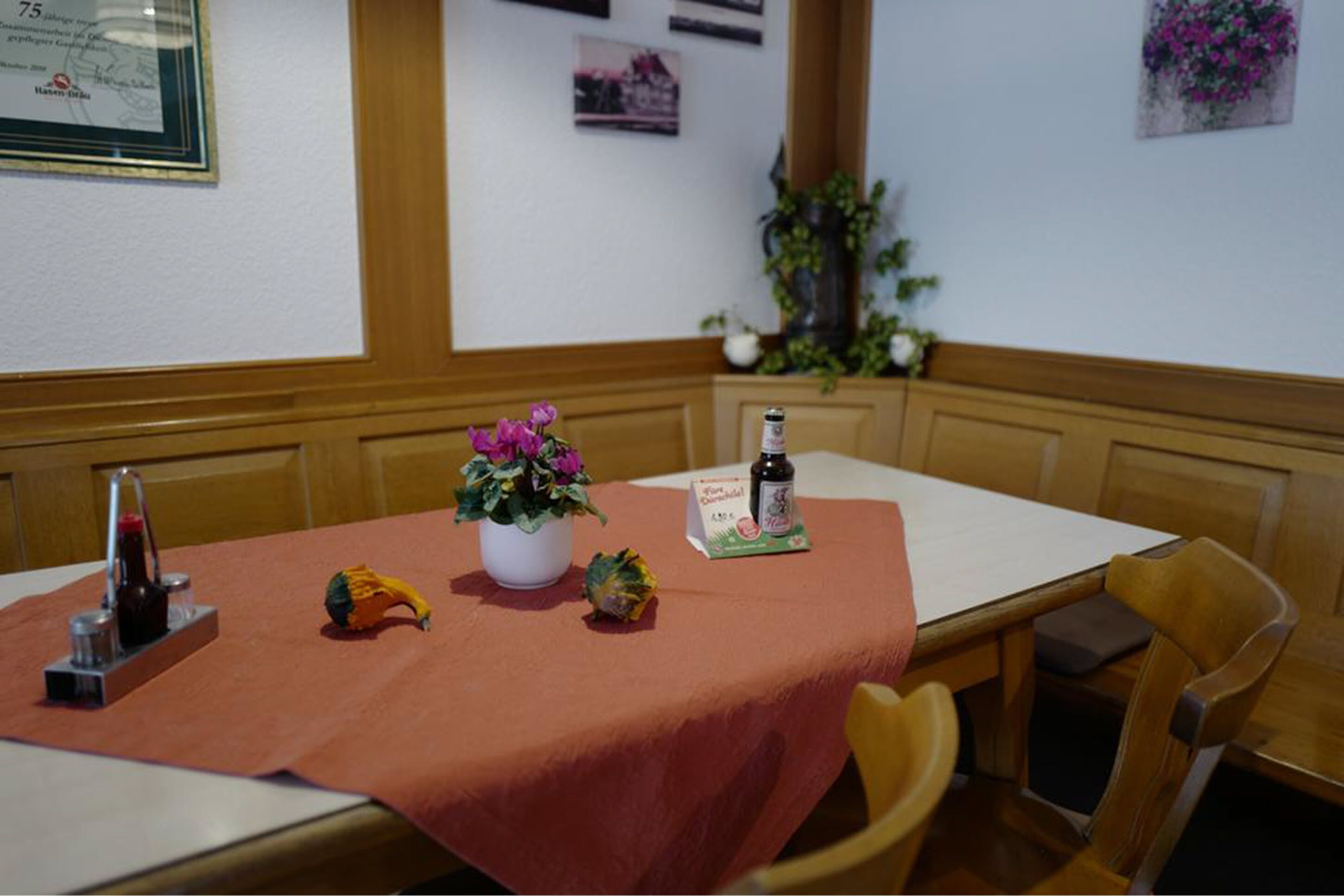 Una mesa de comedor con mantel rojo, una planta en maceta, una botella y un menú.