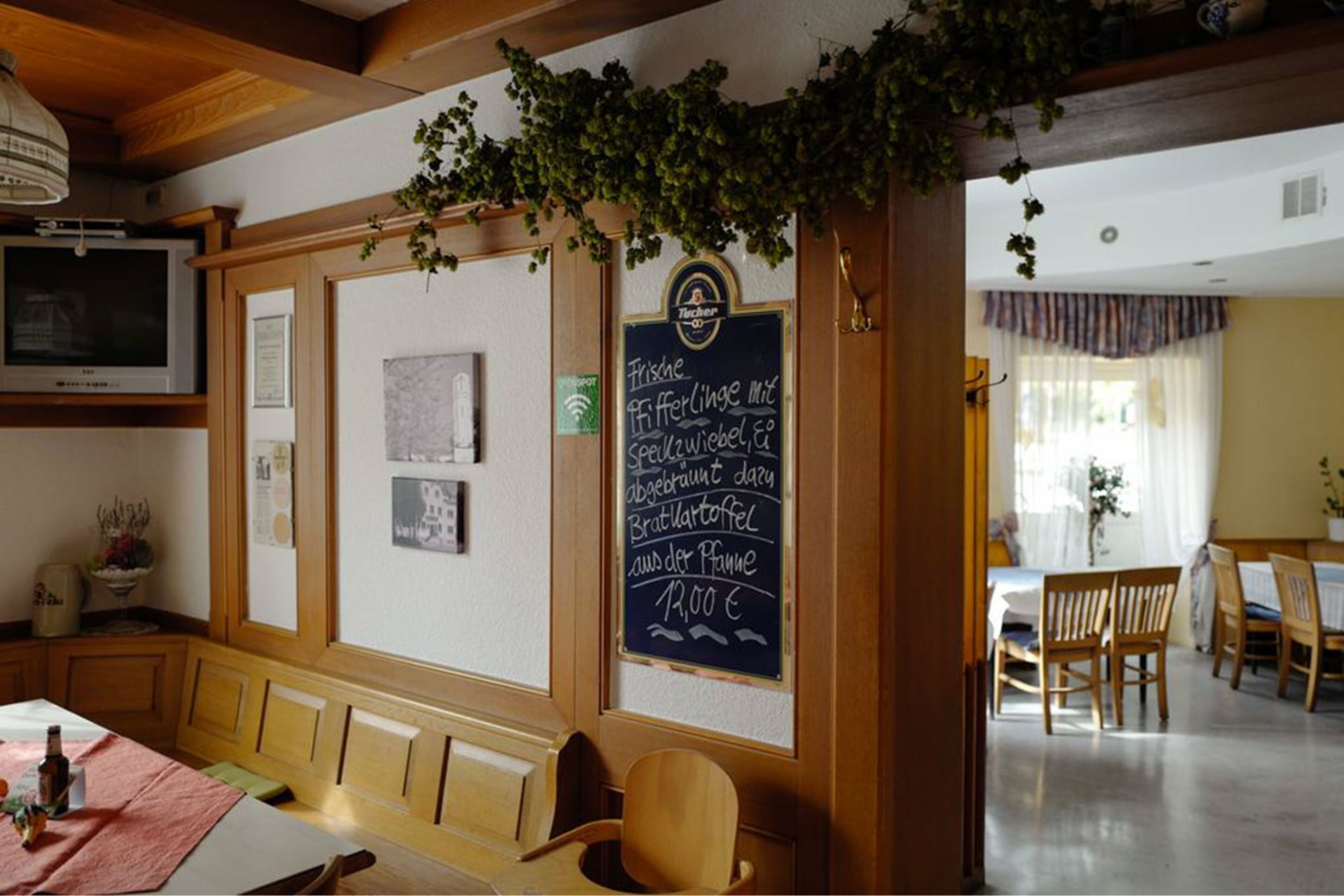 Interior acogedor de un restaurante con muebles de madera, un menú en una pizarra y vista al salón comedor.