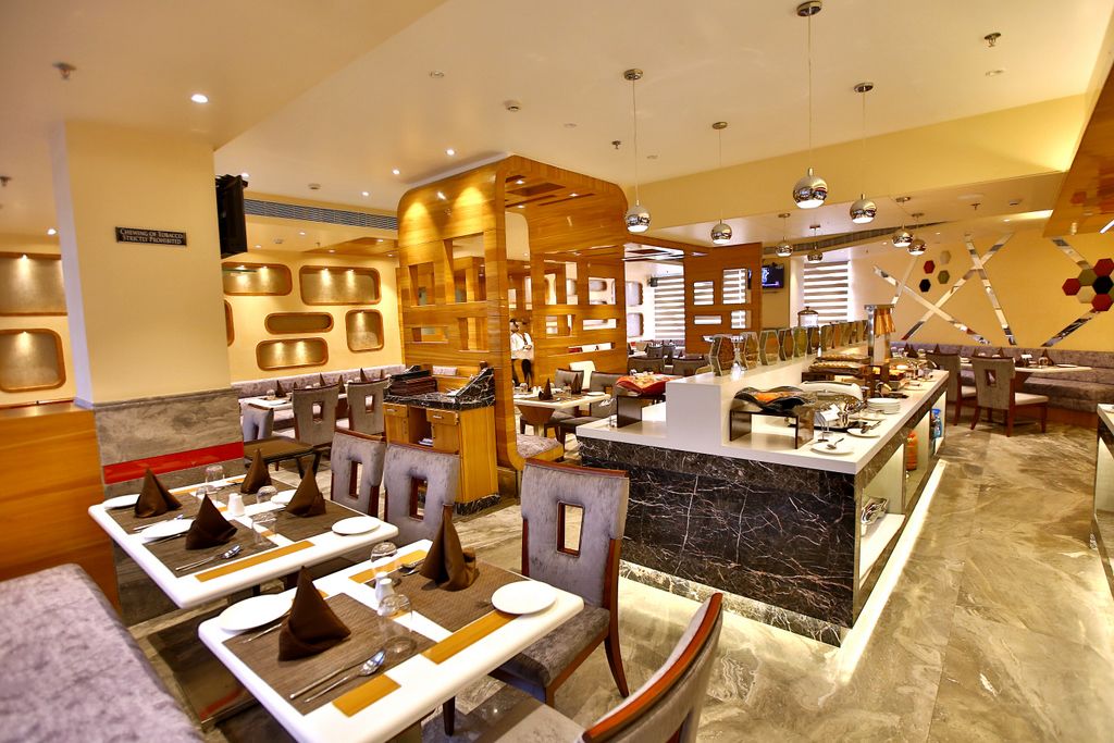 A modern restaurant with multiple dining tables, a central bar area, and a decorative wall with geometric patterns.