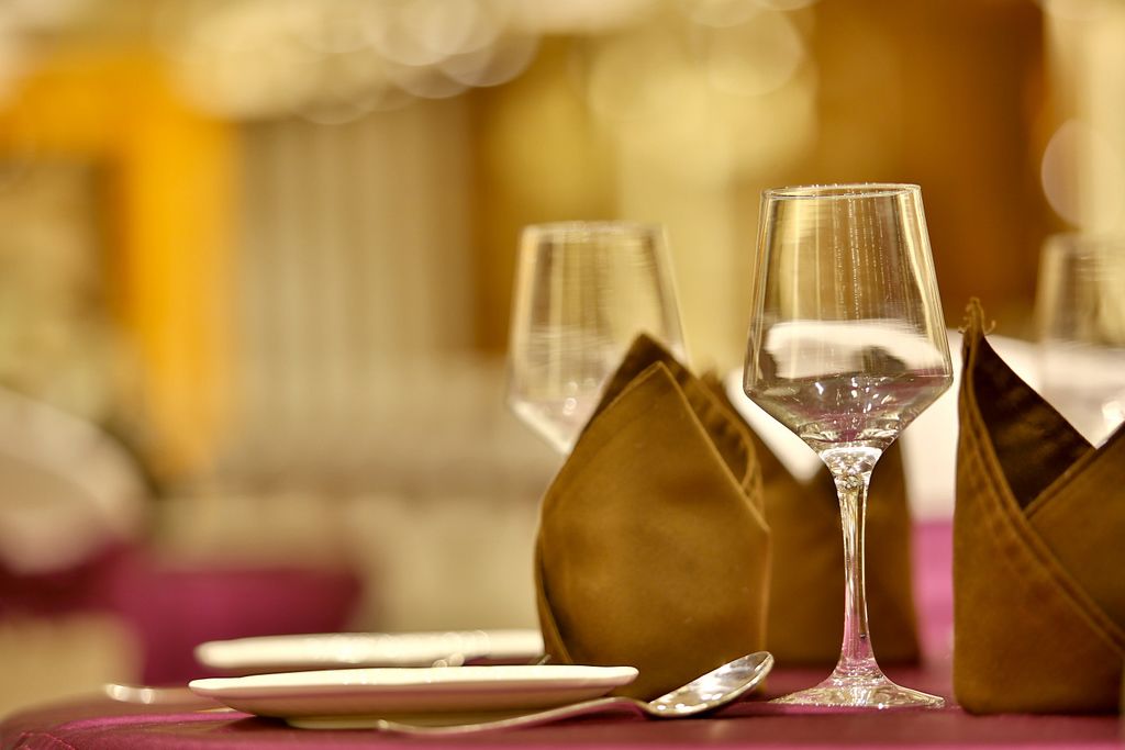 Una mesa servida con cristalería transparente, platos y una cuchara, con un fondo desenfocado que sugiere un ambiente de comedor formal.