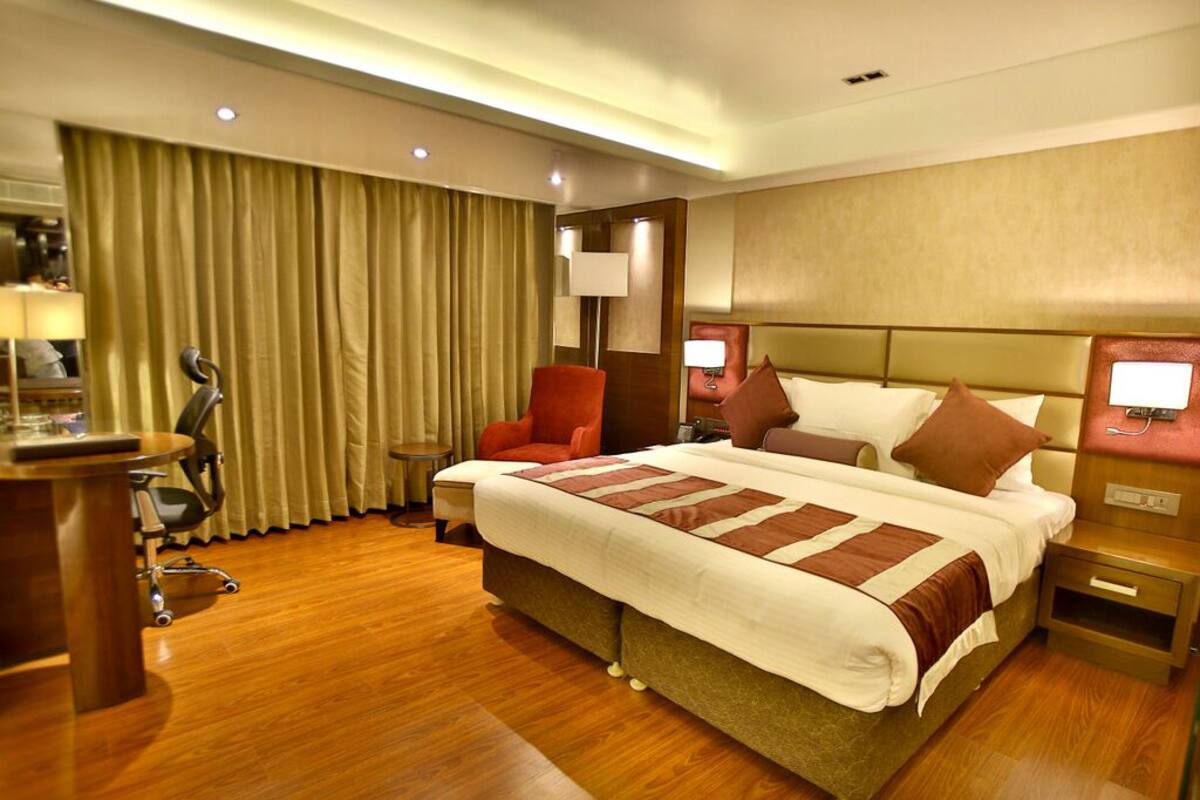 A hotel room with a large bed, a desk, a chair, and a lamp.