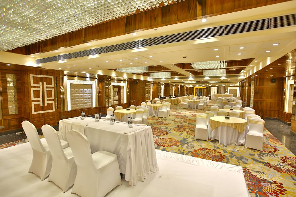 A large banquet hall with round tables and white chairs, wooden paneling, and a patterned carpet.