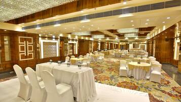 A large banquet hall with round tables and white chairs, wooden paneling, and a patterned carpet.