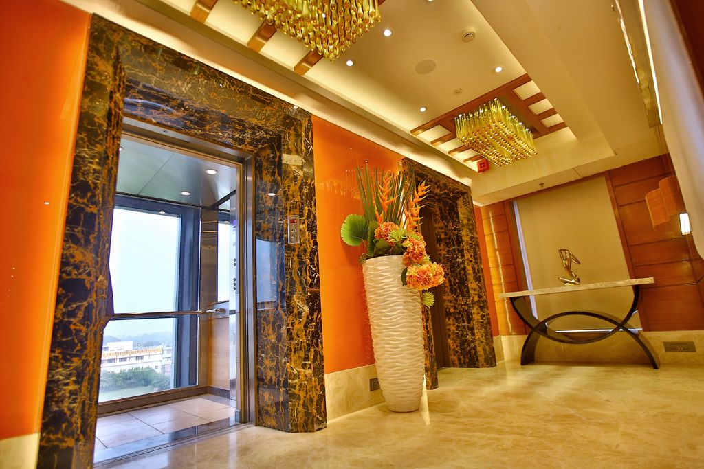 A hotel lobby with a marble reception desk, a large vase with flowers, and a view through the glass doors.