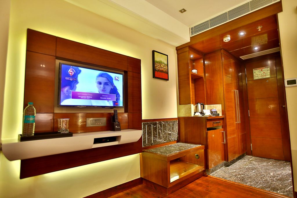 Hotelkamer met een aan een houten paneel bevestigde televisie, een zithoekje en een houten garderobe met spiegel.