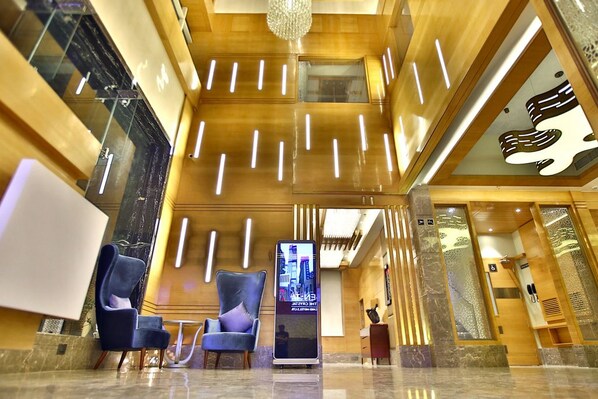 A modern lobby with a chandelier, two blue armchairs, a digital information kiosk, and a reception desk. - Regenta Central The Crystal (Kanpur)