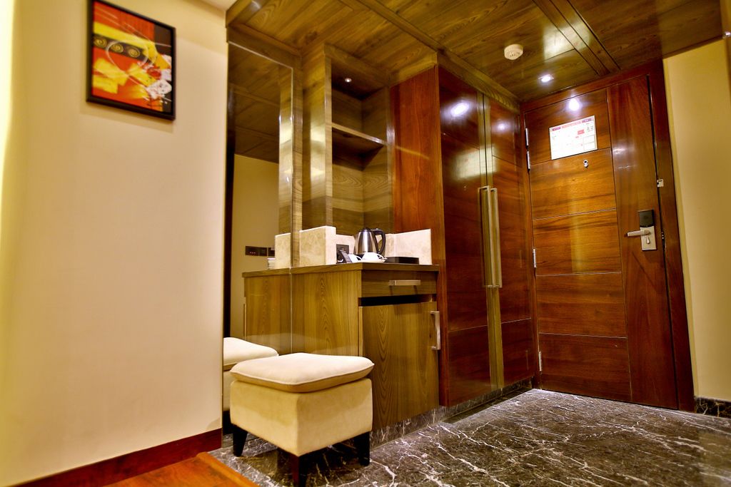 A hotel room with a wooden ceiling, a marble floor, a wooden wardrobe, a small white bench, and a framed picture on the wall.