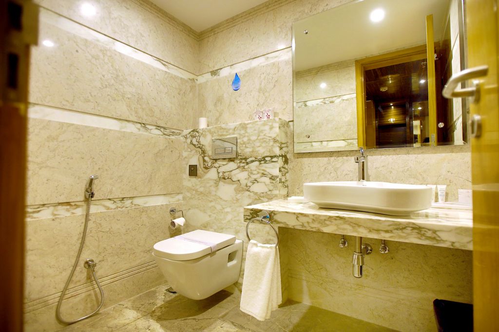A bathroom with a marble wall, a white sink, a toilet, and a shower.