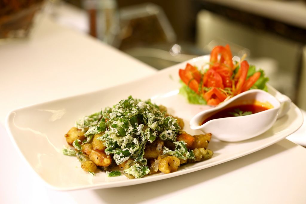 Un plato de comida con vegetales al lado y un pequeño recipiente de salsa.