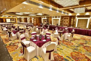 Une salle de banquet avec des tables rondes, des chaises blanches ornées de rubans violets et un sol recouvert de moquette.