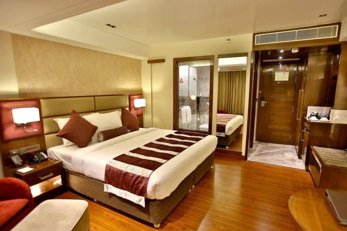 A hotel room with a large bed, bedside tables, a desk, a chair, a mirror, and a bathroom visible through an open door.