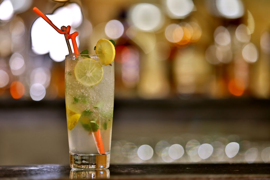 A tall glass with a lime slice, mint leaves, and an orange straw, set against a blurred background with bokeh lights.