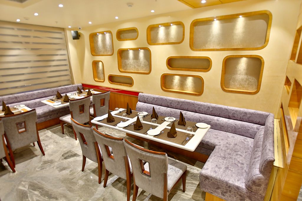 Un restaurant avec une longue table dressée pour un repas, des sièges confortables et un mur décoratif orné d’ouvertures rectangulaires.
