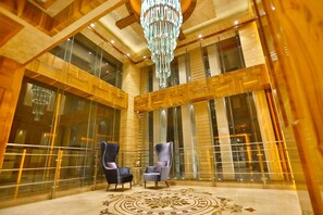 A spacious lobby with high ceilings, a large chandelier, and two armchairs. - Regenta Central The Crystal (Kanpur)