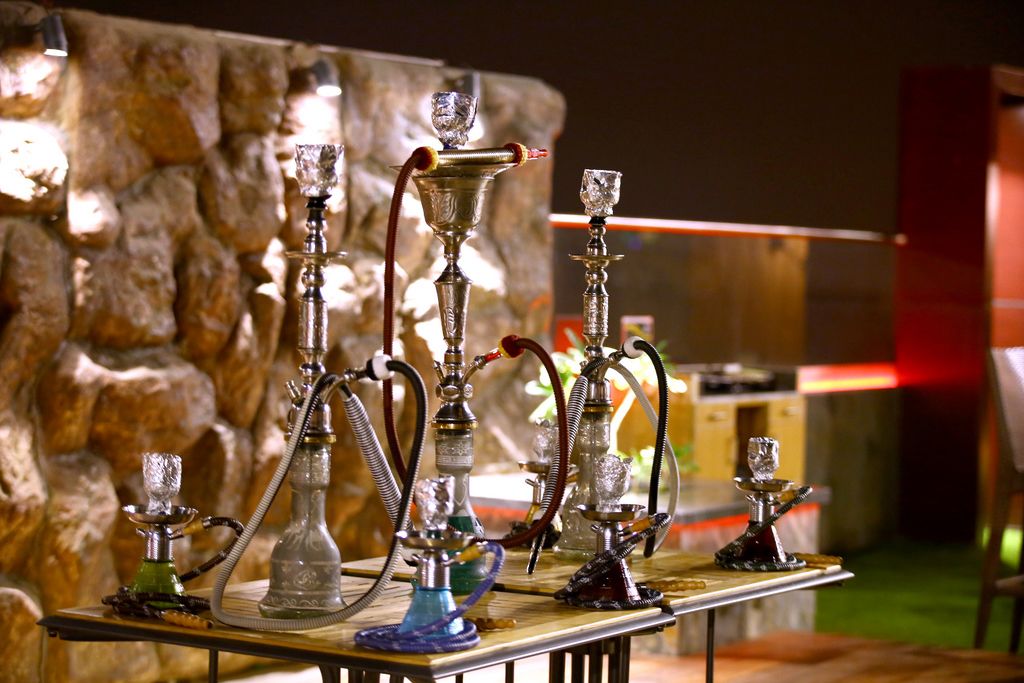 A variety of hookahs on a wooden table with a stone wall in the background.