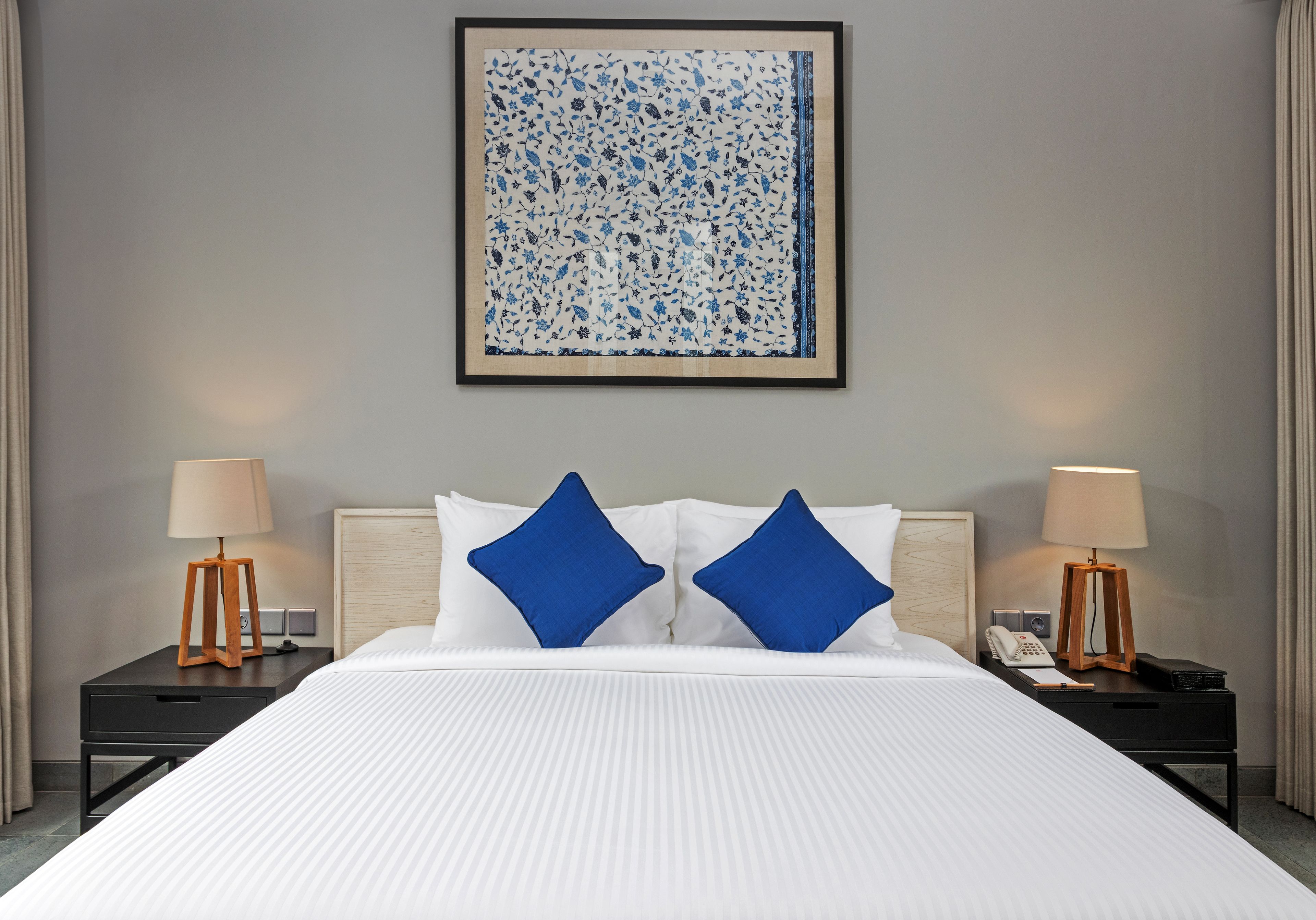 A hotel room with a large bed, two nightstands, a lamp, a telephone, and a framed artwork on the wall.