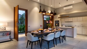 A modern kitchen with a central island, pendant lighting, and a dining area with a table set for four. - Amarin Seminyak (Seminyak)