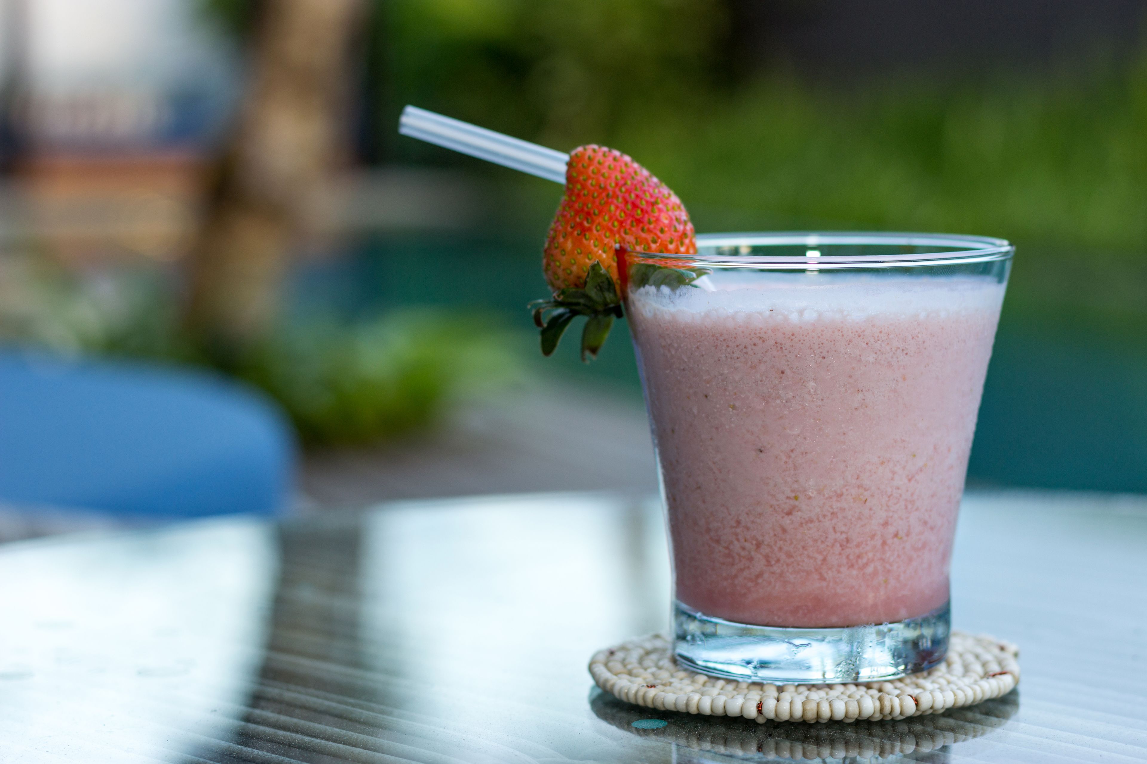A glass of pink smoothie with a strawberry on the rim, placed on a coir coaster.