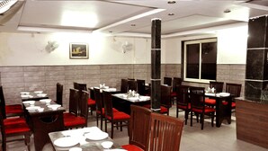 A restaurant with multiple tables and chairs, a large pillar, and a window. - Jagdish Residency (Reasi)
