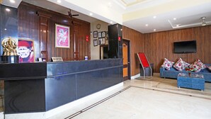 A reception area with a marble floor, a reception desk, a blue sofa, and a television mounted on the wall. - Jagdish Residency (Reasi)