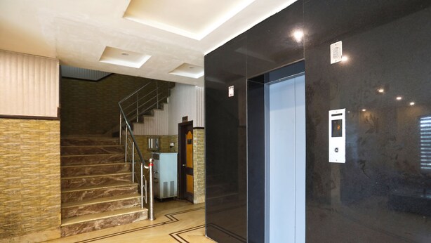A modern elevator with a digital display, a marble staircase, and a wall with a textured pattern. - Jagdish Residency (Reasi)