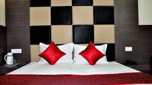 A hotel room with a checkered headboard, two red pillows, a white bedspread, and a red throw blanket. - Jagdish Residency (Reasi)