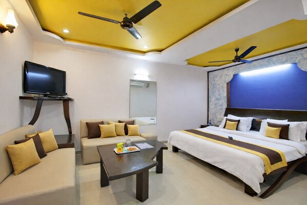 Habitación de hotel con cama, sofá, televisor y ventiladores de techo.