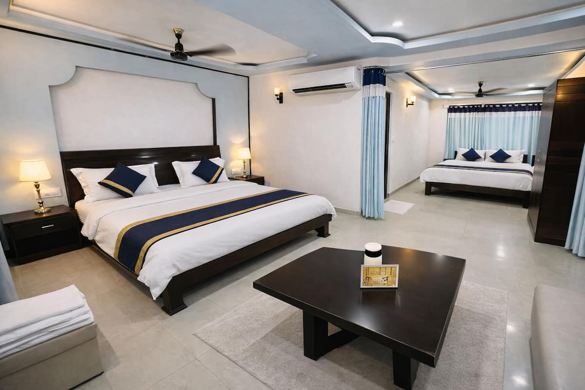 A hotel room with a large bed, a smaller bed, a coffee table, and a nightstand with a lamp.