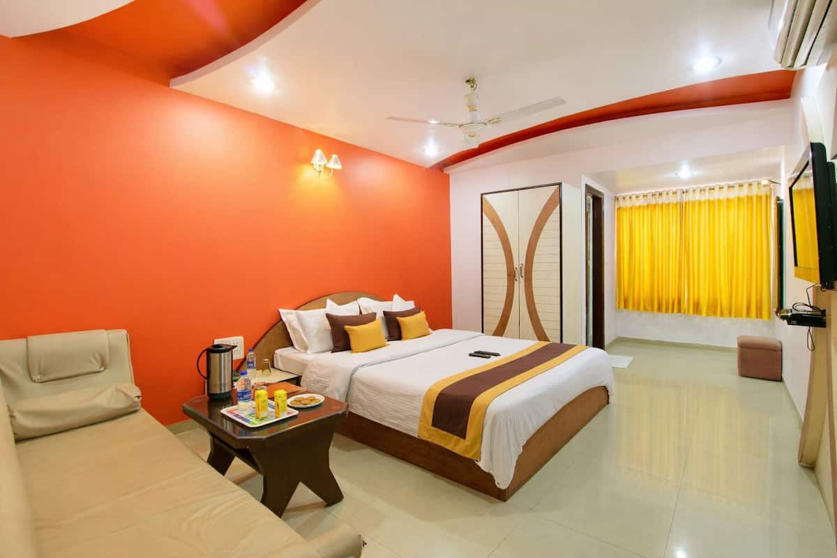 A hotel room with a bed, a desk with a chair, a bedside table with a lamp, a wardrobe, and a television.