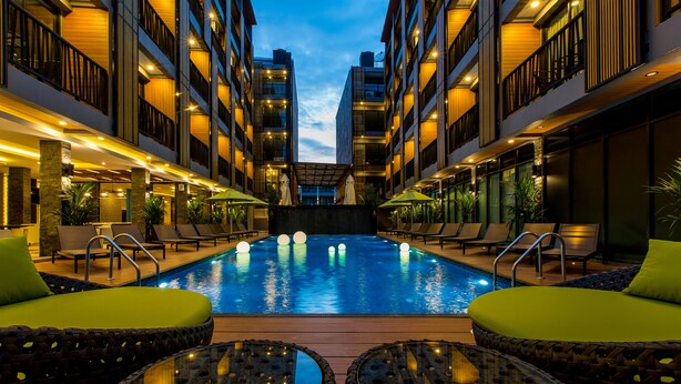Una piscina con sillas y mesas de descanso, rodeada de edificios de varios pisos con balcones.