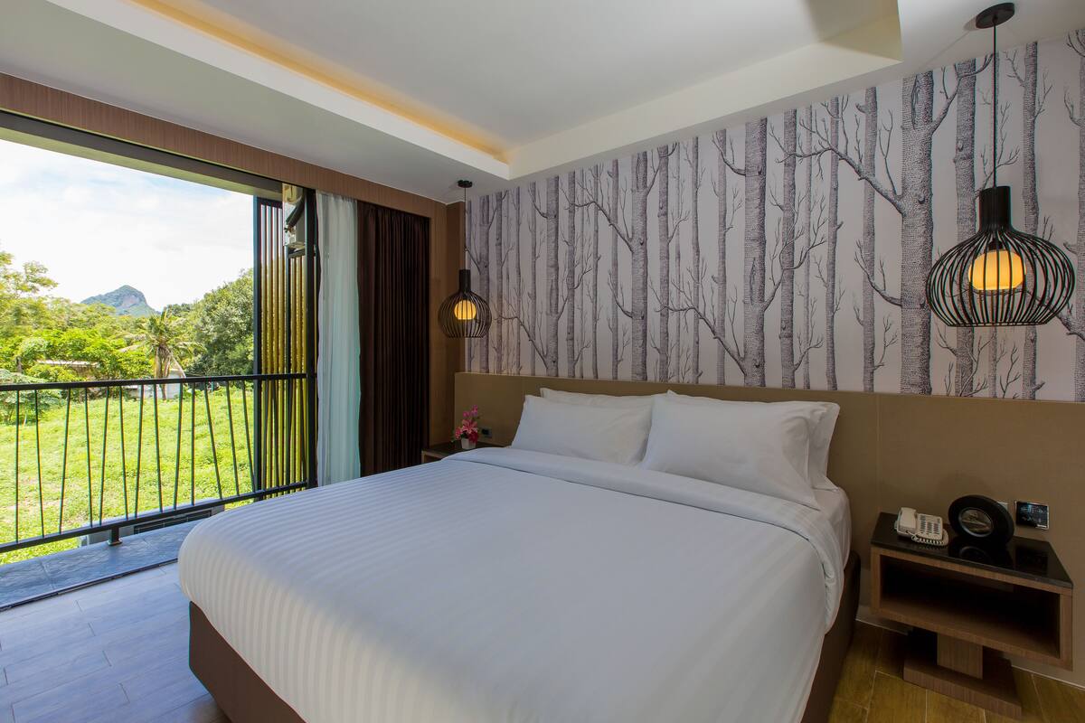 A hotel room with a large bed, a view of greenery, and a wall with a tree pattern.
