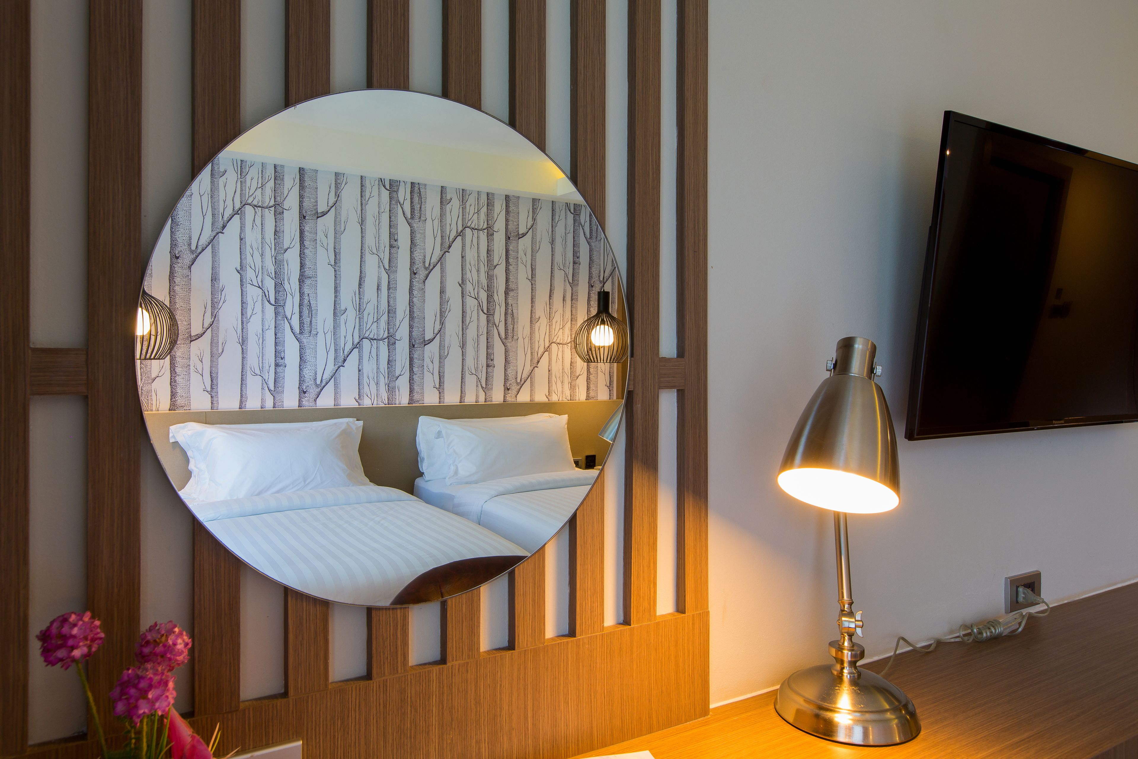 Hotelkamer met ronde spiegel, waarin een bed, een wandtelevisie en een bedlampje weerspiegeld worden.