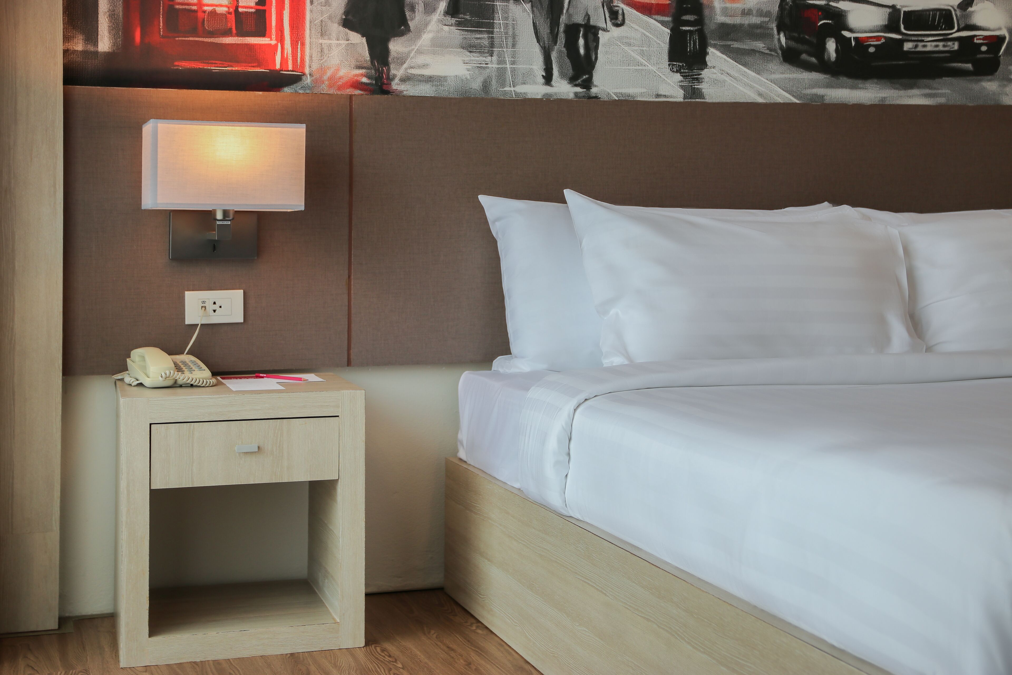 Une chambre d’hôtel avec un lit, une table de chevet avec une lampe et un téléphone fixé au mur.