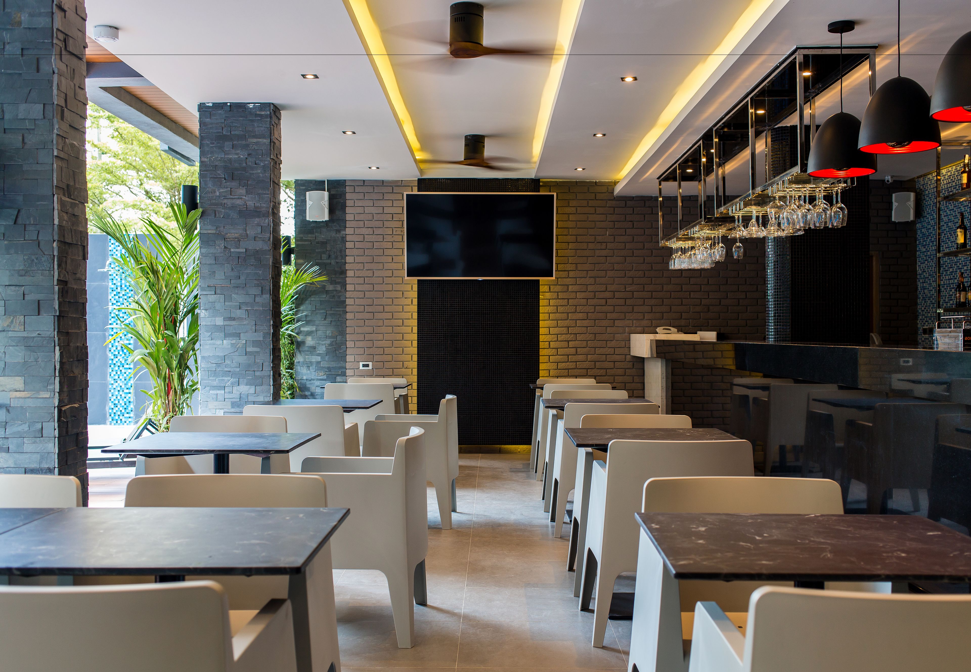 Un restaurante con una decoración moderna, que presenta paredes de ladrillo, sillas blancas y una zona de bar con luces colgantes.