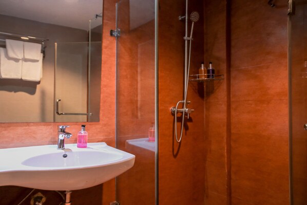 Un baño con lavamanos blanco, un espejo y una zona de ducha con paredes de vidrio.