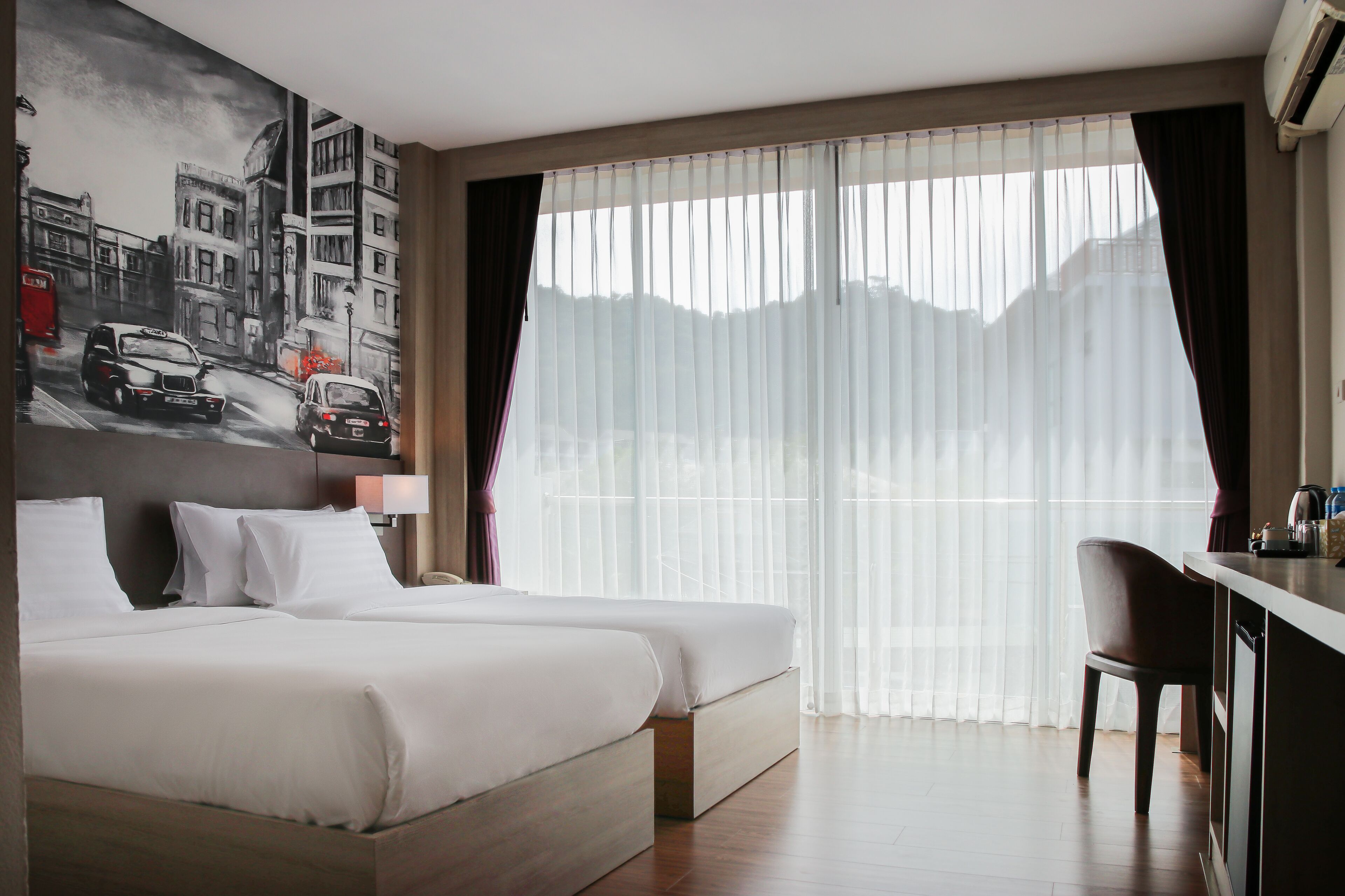 Una habitación de hotel con una cama, un escritorio y un ventanal con cortinas traslúcidas.