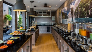 Una cocina moderna con una encimera larga, lámparas colgantes negras y un mural de paisaje tropical.