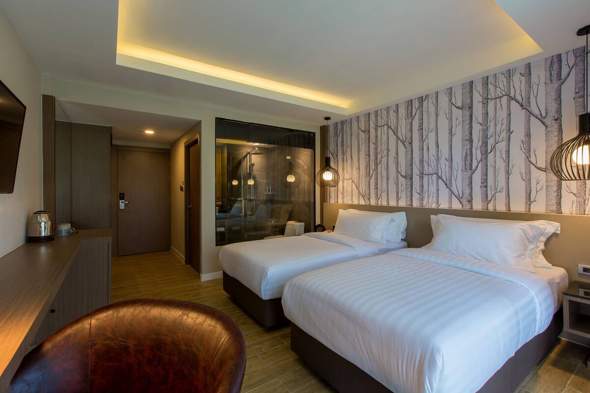 A hotel room with two beds, a seating area, a mirror, and a wall with a tree pattern.