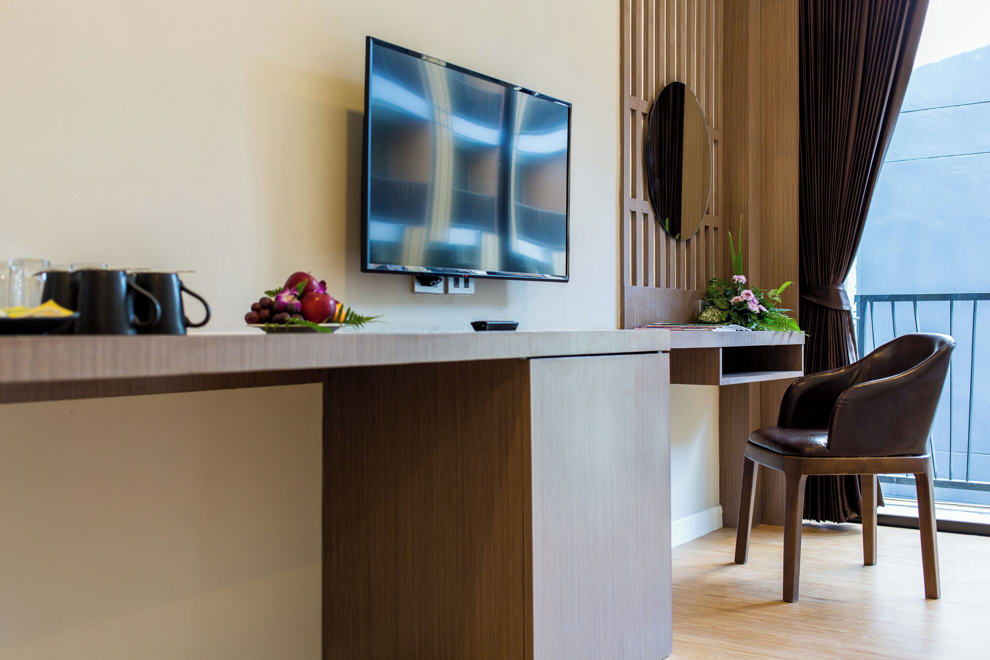 A modern room with a flat-screen TV, a wooden desk, a chair, and a balcony with curtains.