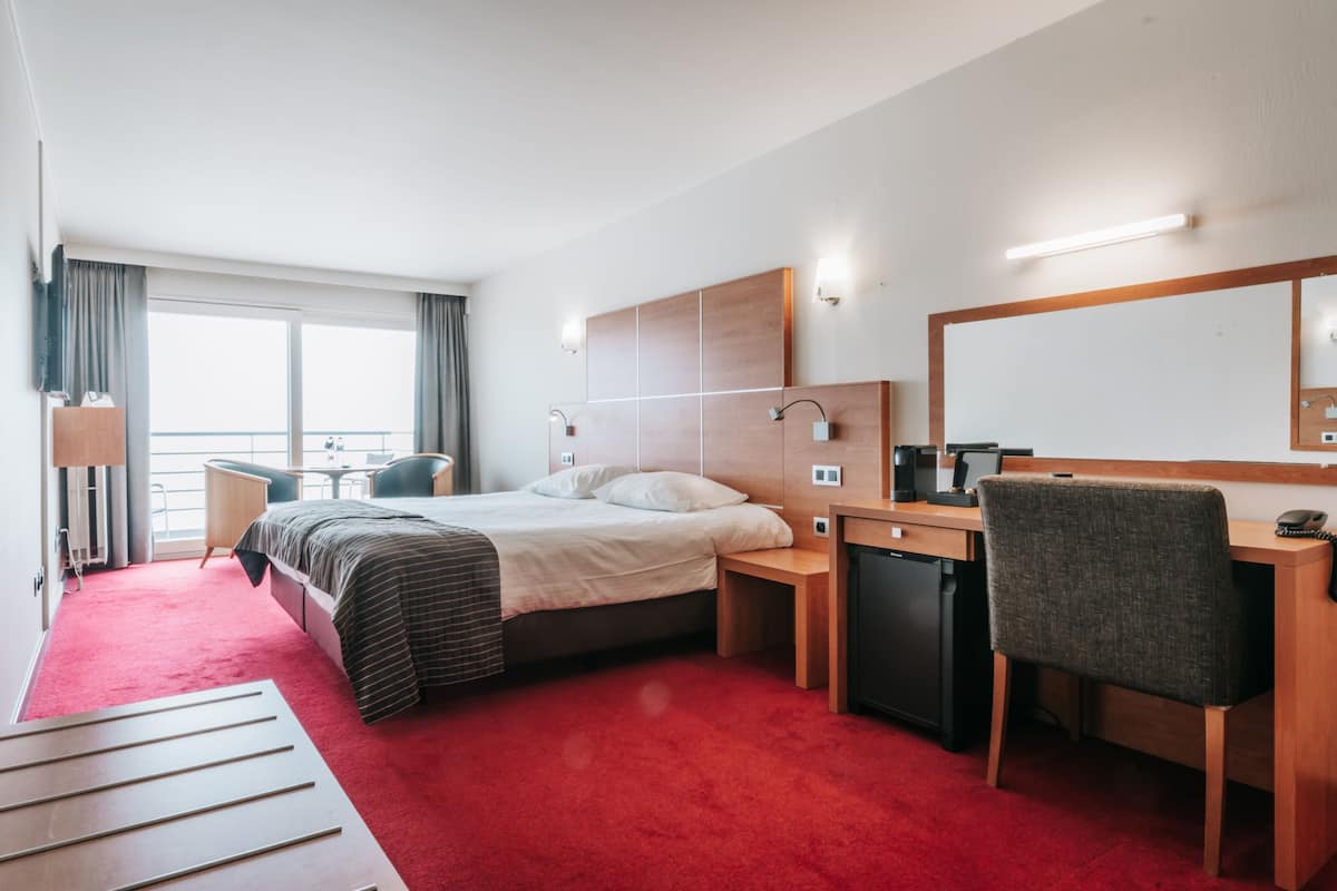 A hotel room with a bed, desk, chair, and a large window.