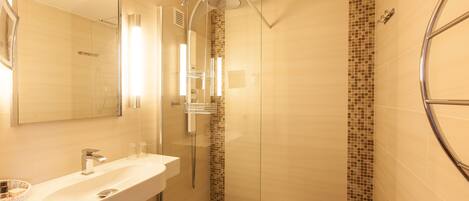 A modern bathroom with a glass-enclosed shower, a white sink with a mirror, and a tiled shower wall.