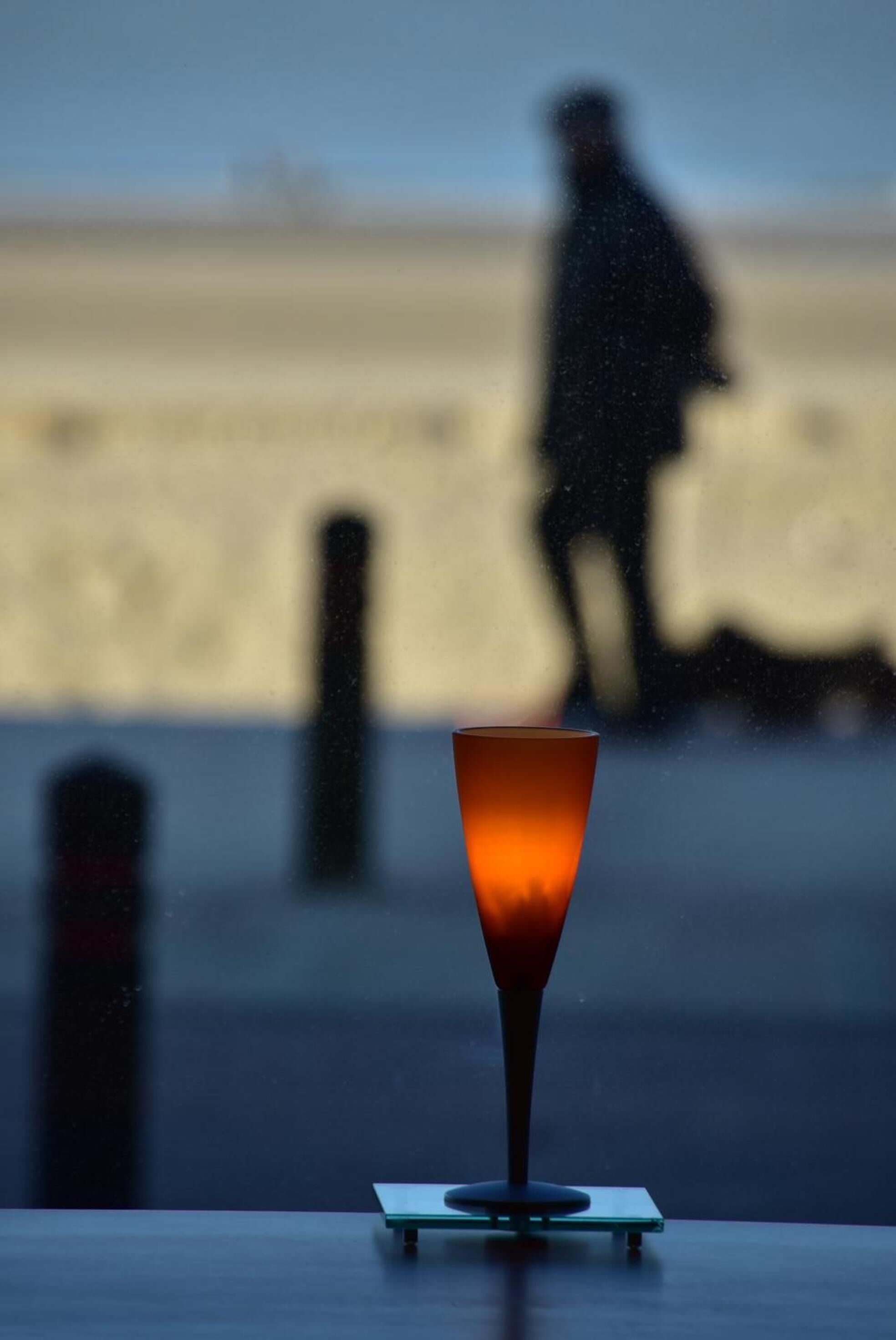 Un verre rempli de boisson sur une table, avec en arrière-plan, flou, une personne qui marche.